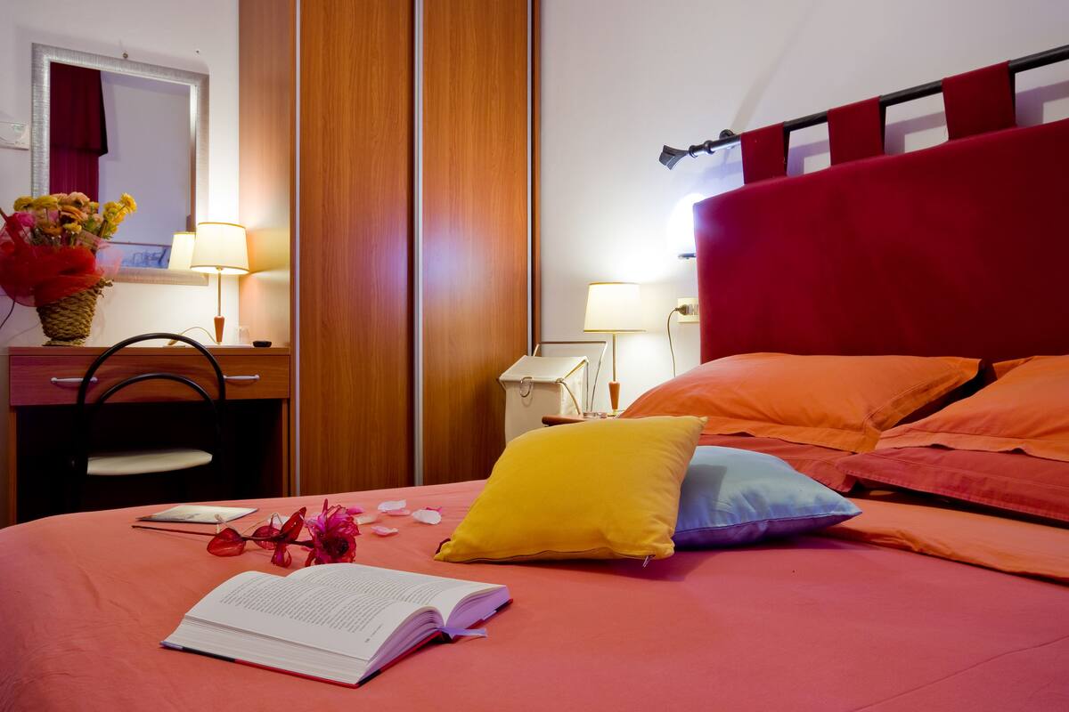 A hotel room with a bed, a desk, a chair, a lamp, and a mirror.