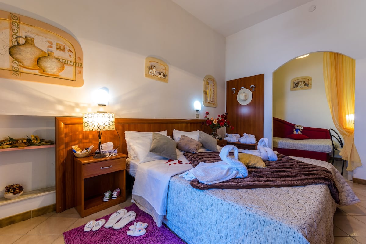 A hotel room with a bed, a nightstand, a lamp, a mirror, and a shower area.