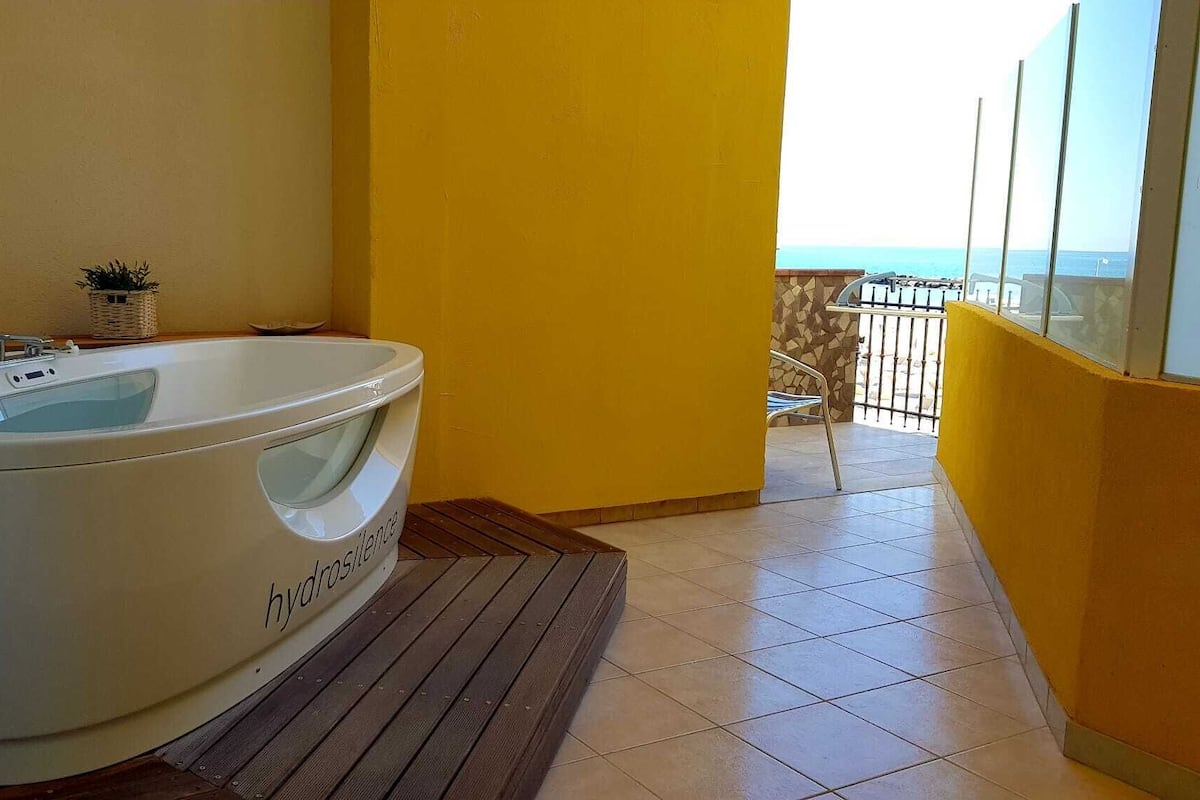 A bathroom with a large bathtub, a small potted plant, and a view of the ocean through a balcony.