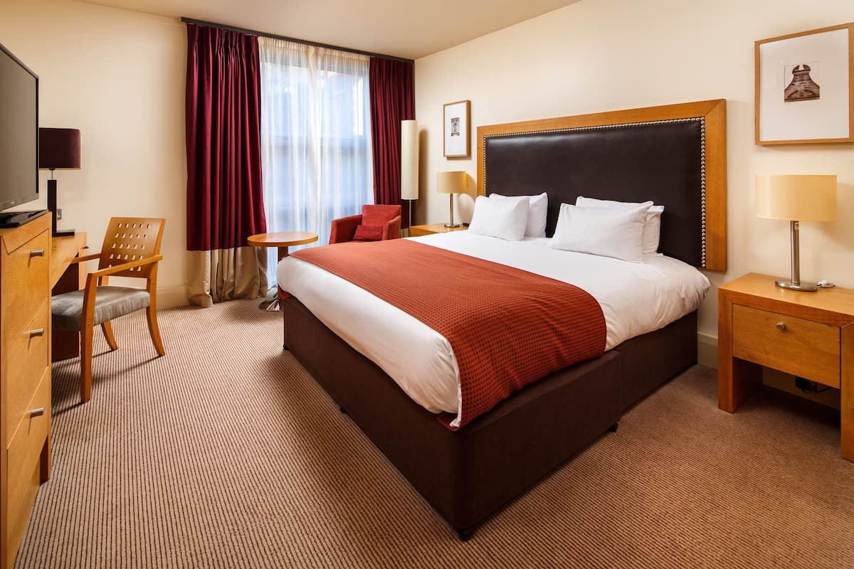 A hotel room with a large bed, a desk, a chair, a TV, and a window with curtains.