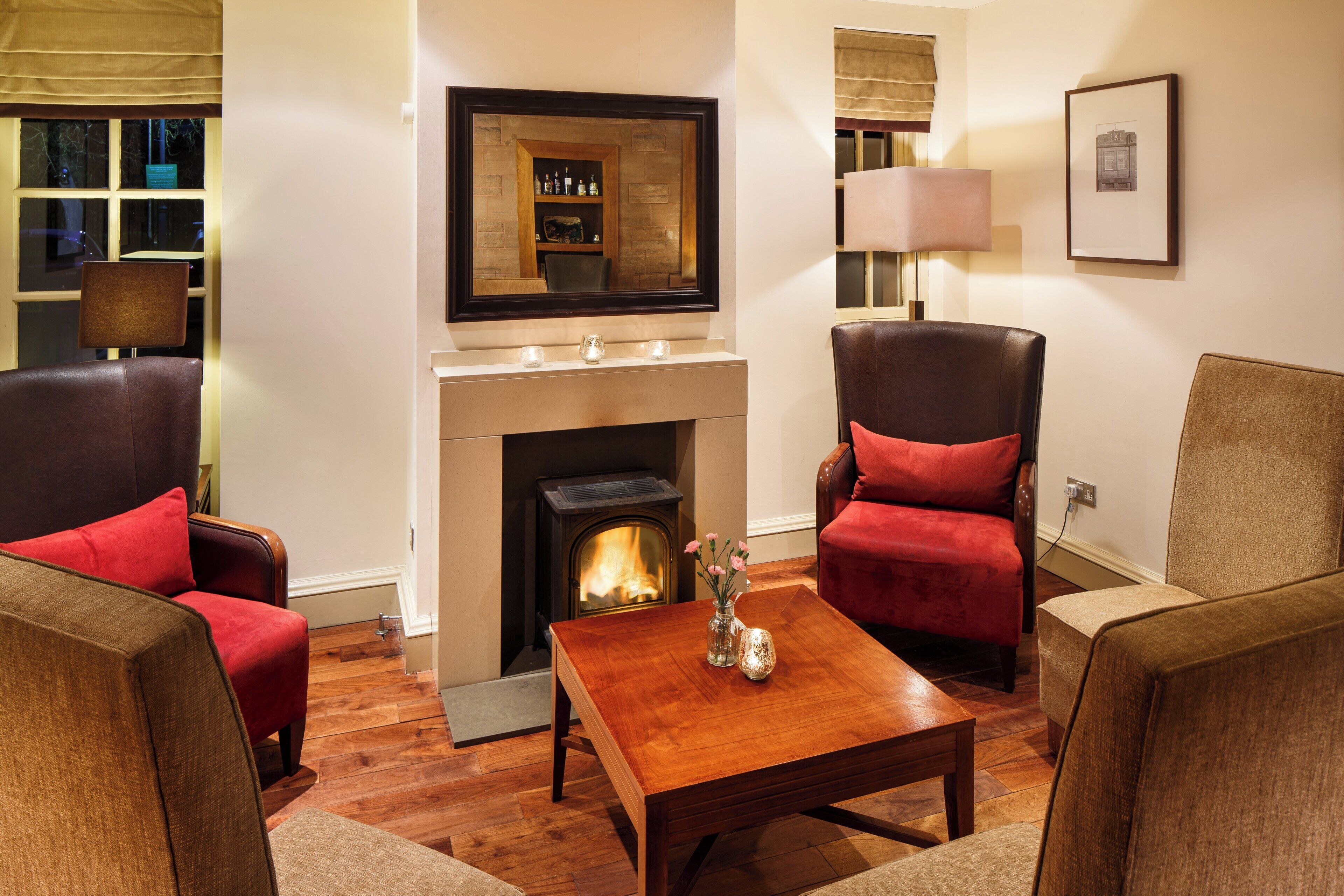 A cozy living room with a fireplace, leather armchairs, a wooden coffee table, and a framed picture on the wall.