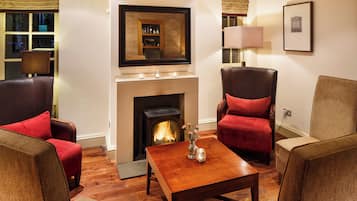 A cozy living room with a fireplace, leather armchairs, a wooden coffee table, and a framed picture on the wall.