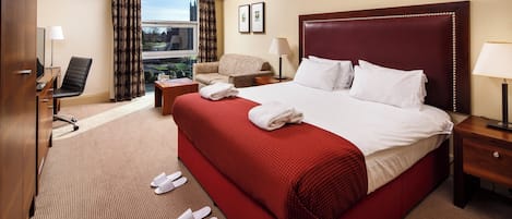 A hotel room with a large bed, a desk with a chair, a sofa, and a window with curtains.