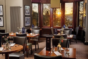 A restaurant interior with multiple dining tables, chairs, and framed artwork on the walls. - Holiday Inn Dumfries by IHG (Dumfries)