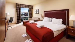 A hotel room with a large bed, a desk, a chair, a window with curtains, and a view of the outdoors.