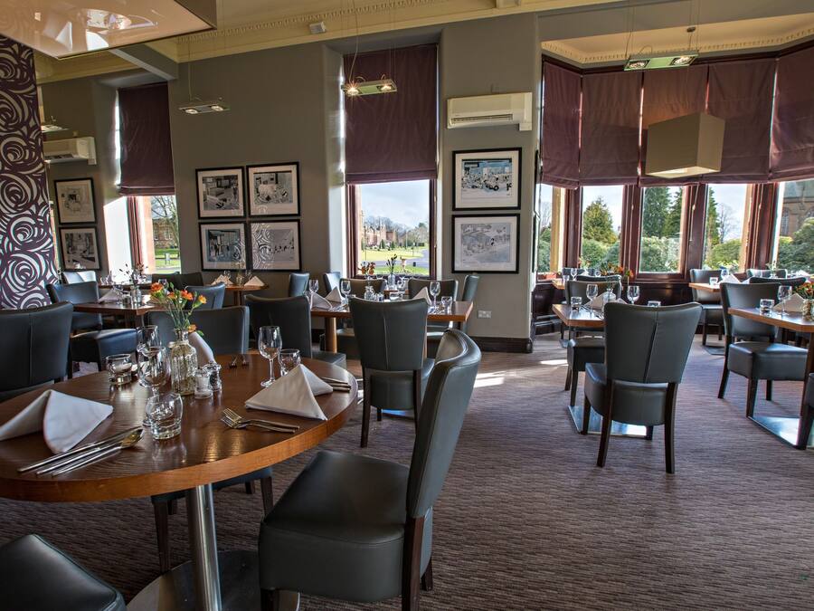 A restaurant with multiple tables set for dining, framed artwork on the walls, and large windows offering a view of the outdoors.
