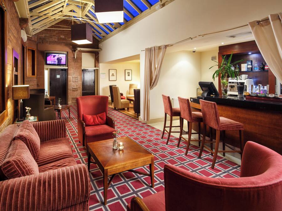 A hotel lobby with a bar area, seating arrangements, and a television screen.