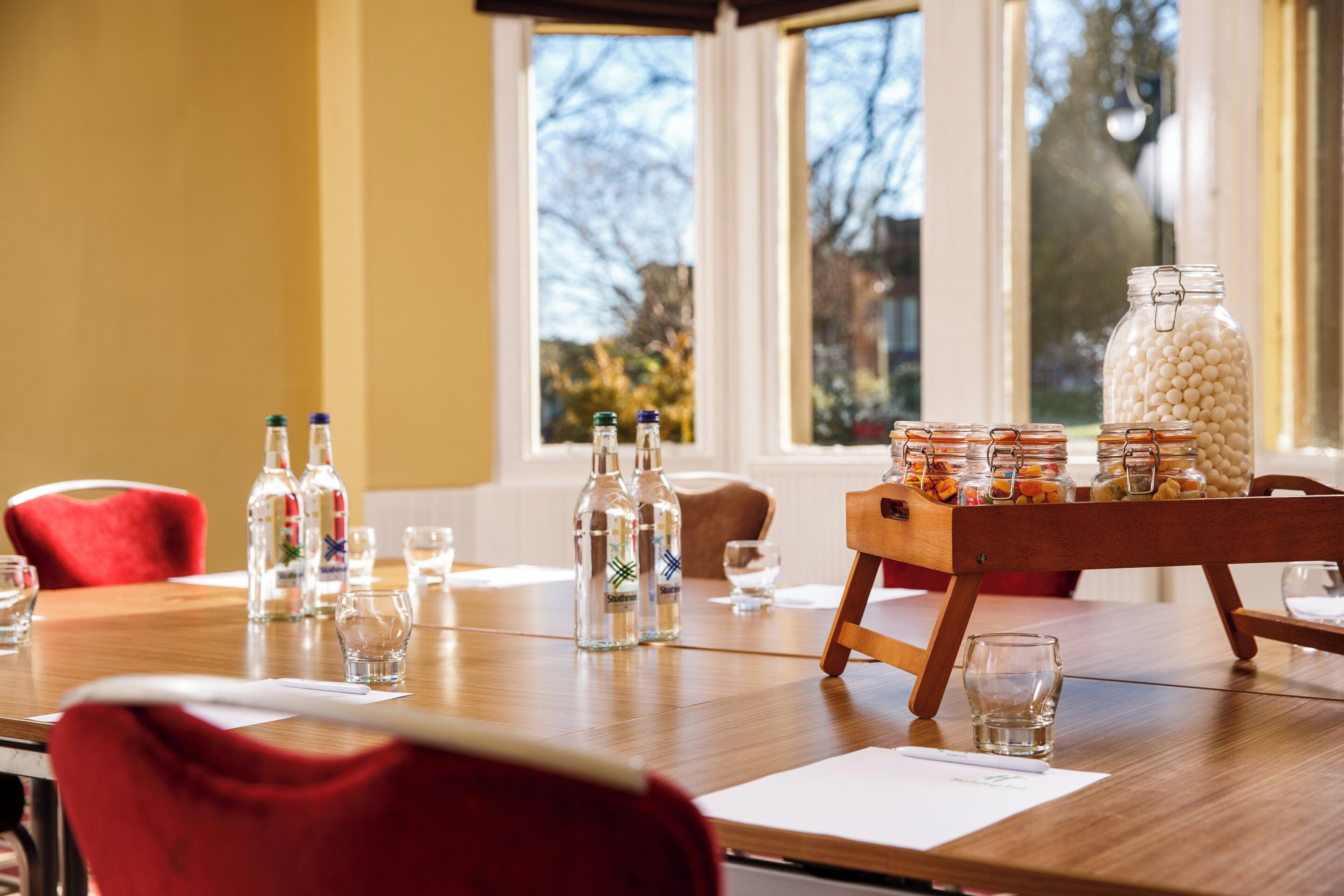 A dining table with clear glasses, bottles, and a wooden tray with jars.