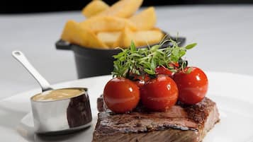 A plate with a steak, cherry tomatoes, and a small bowl of sauce.