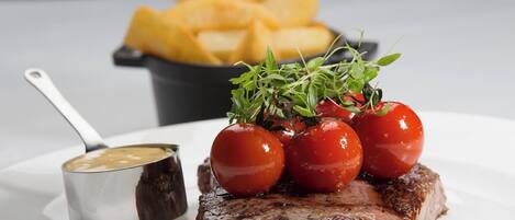 A plate with a steak, cherry tomatoes, and a small bowl of sauce.