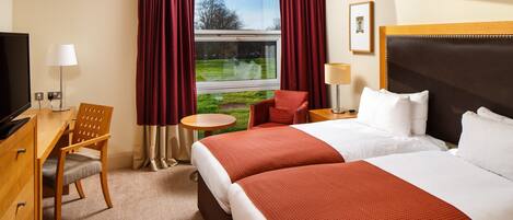 A hotel room with two beds, a desk, a chair, a TV, and a window with curtains.