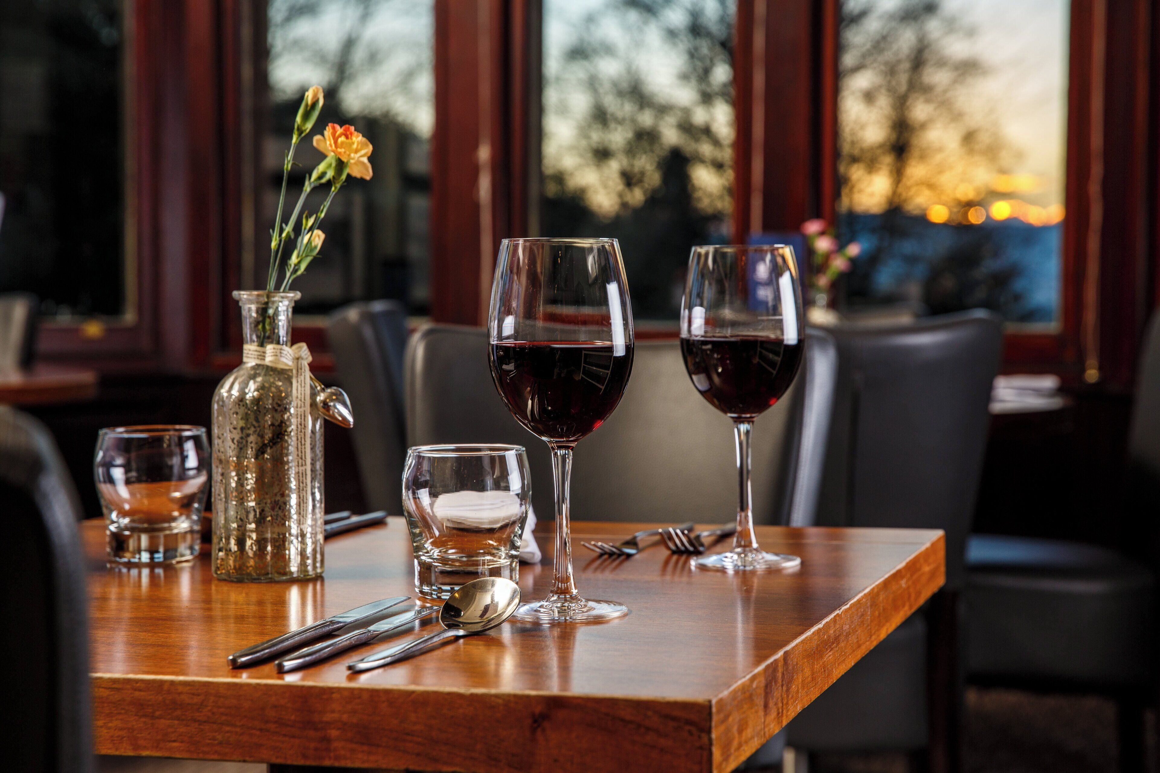 A dining table with a vase of flowers, two wine glasses, a glass of water, and cutlery.