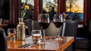 Une table à manger avec un vase de fleurs, deux verres à vin, un verre d’eau et des couverts.