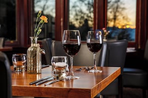 Una mesa de comedor con un jarrón de flores, dos copas de vino, un vaso de agua y cubiertos.
