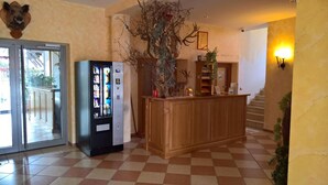 A lobby with a vending machine, a wooden reception desk, a mounted deer head, and a staircase.