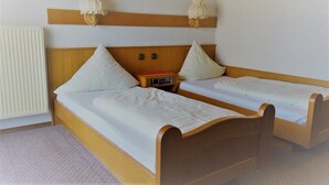 A room with two single beds, wooden headboards, a bedside table with a radio, and a radiator.