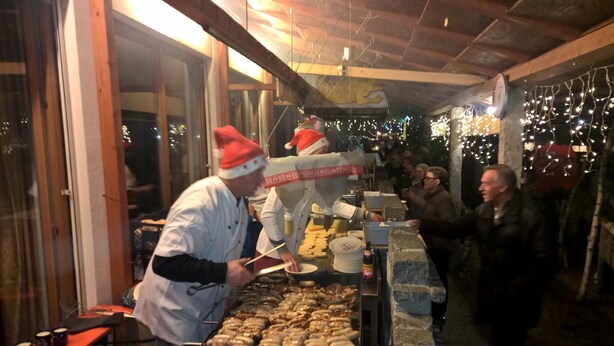 A food stall with a person serving food, a counter with food items, and a crowd of people.