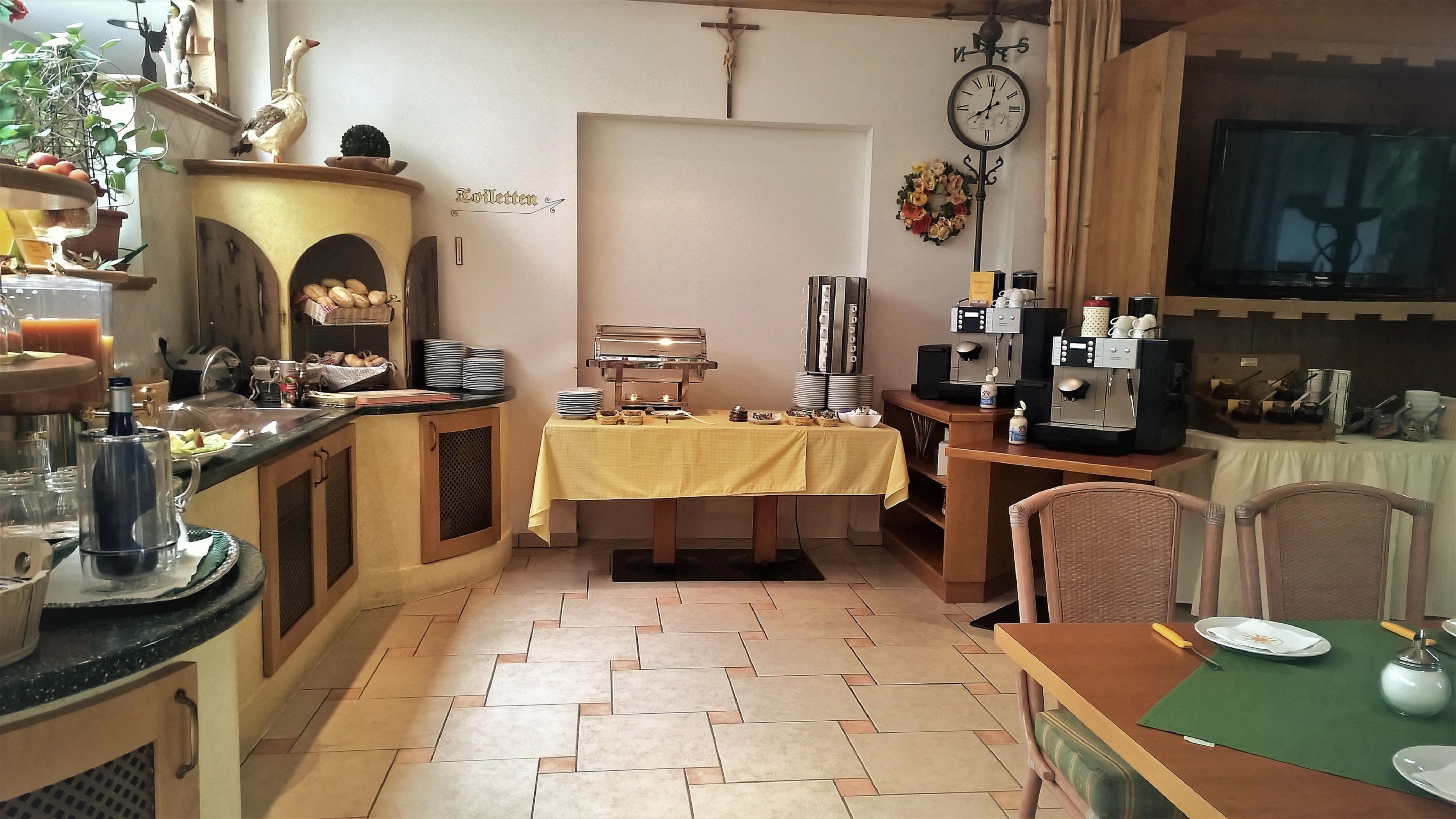 A small, cozy room with a buffet setup, a clock on the wall, and a cross above the door.