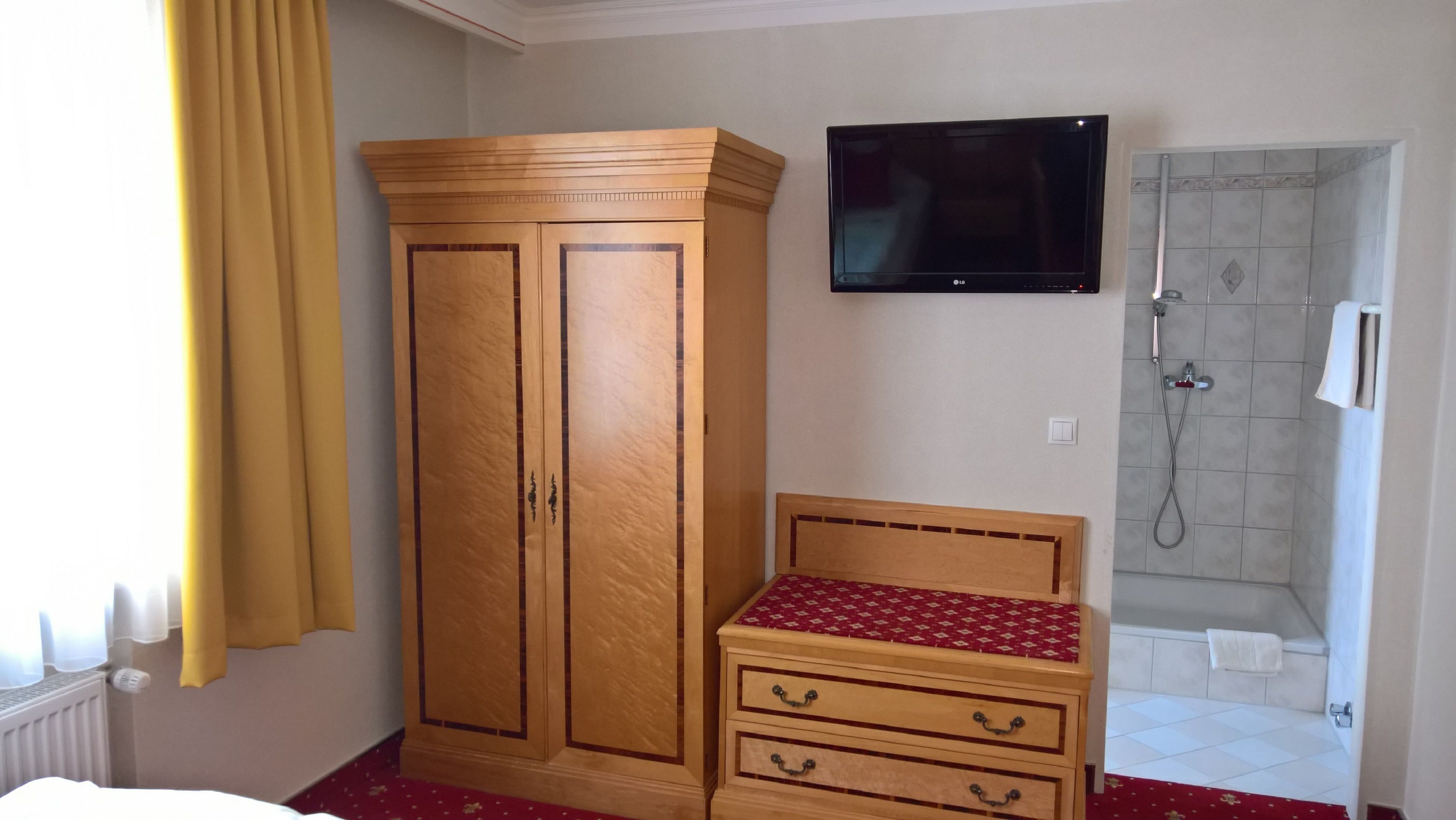 A hotel room with a wardrobe, a television, a small bedside table, and a shower area.