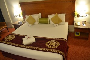 A neatly made bed with a patterned bedspread, pillows, and a bedside table with a lamp and a phone. - Ramee Guestline Hotel (Dubai)