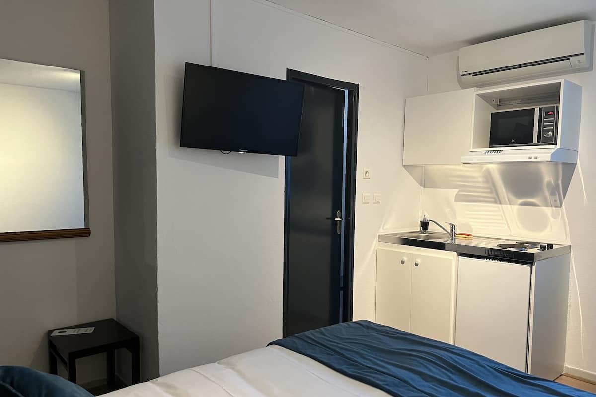 Un dormitorio pequeño con cama, televisión montada en la pared, microondas y una kitchenette.