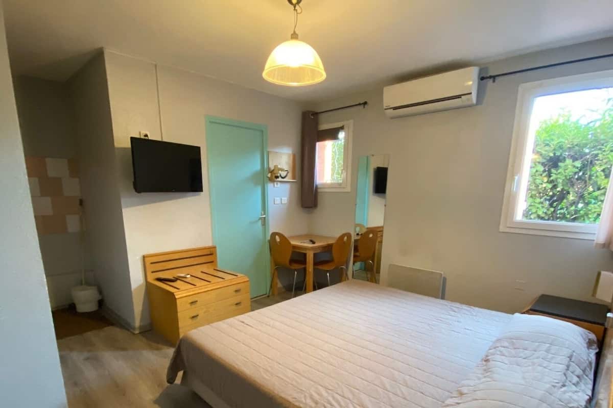 Un dormitorio con cama, escritorio y silla. Se ve follaje verde a través de la ventana.