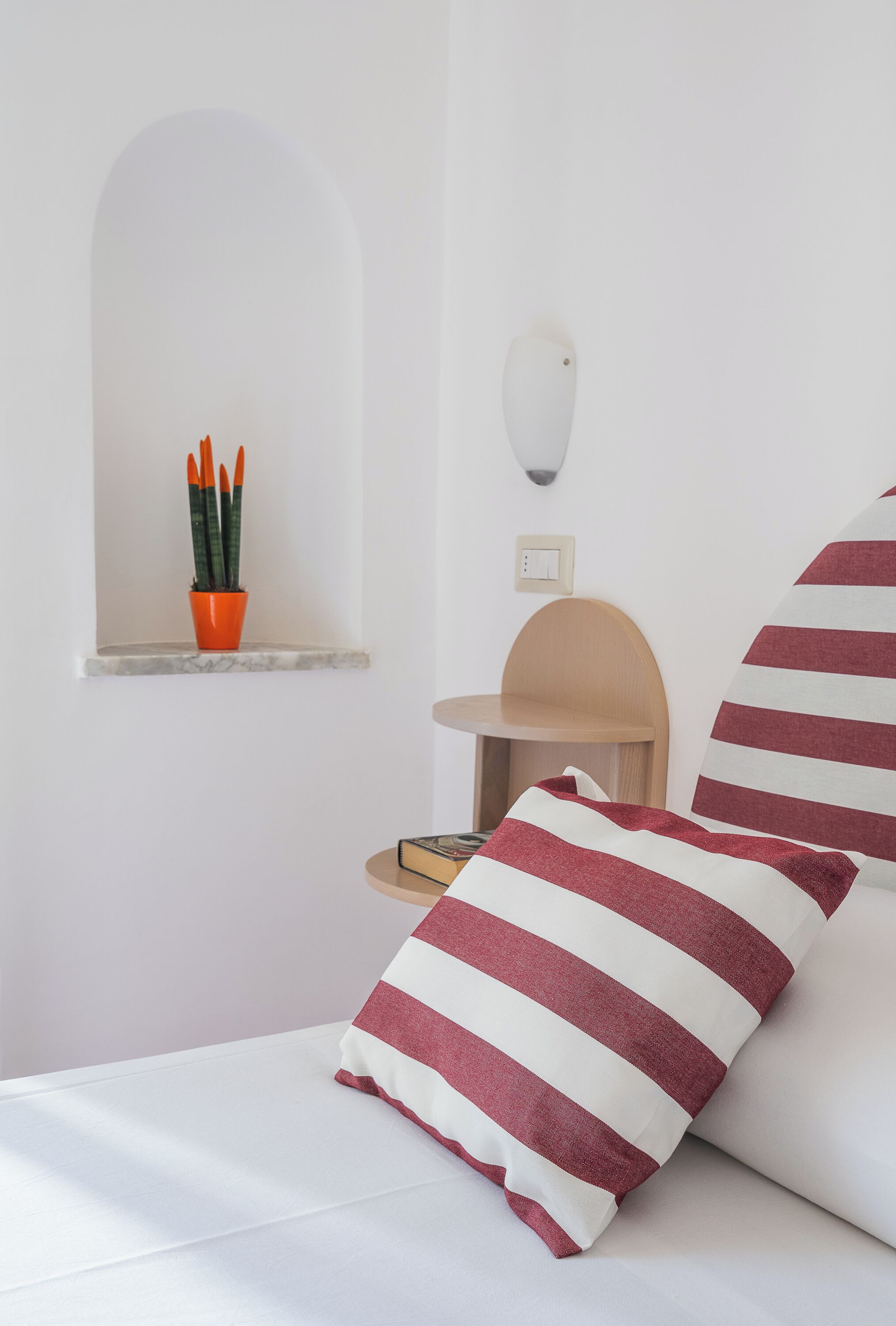 Una cama con almohadas a rayas, un estante pequeño con una planta en maceta y una mesa redonda con una silla.