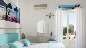 Quarto com cama, escrivaninha, cadeira, espelho e vista para o exterior.