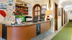 Uma receção com bancada em madeira, um computador portátil e um vaso com flores vermelhas.