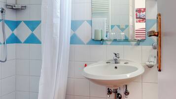Un baño con ducha, lavamanos y espejo.