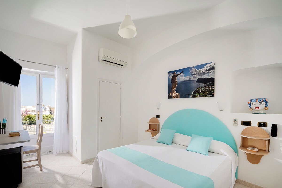 A bedroom with a bed, a desk, a chair, a door, and a window.
