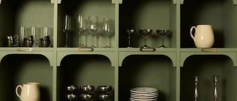 A green cabinet with multiple shelves containing various glassware and dishes.