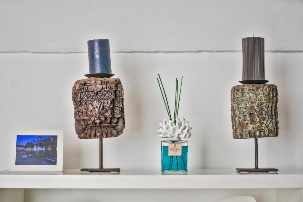 Three decorative items on a shelf: a textured sculpture, a vase with green stems, and a bottle with a label.