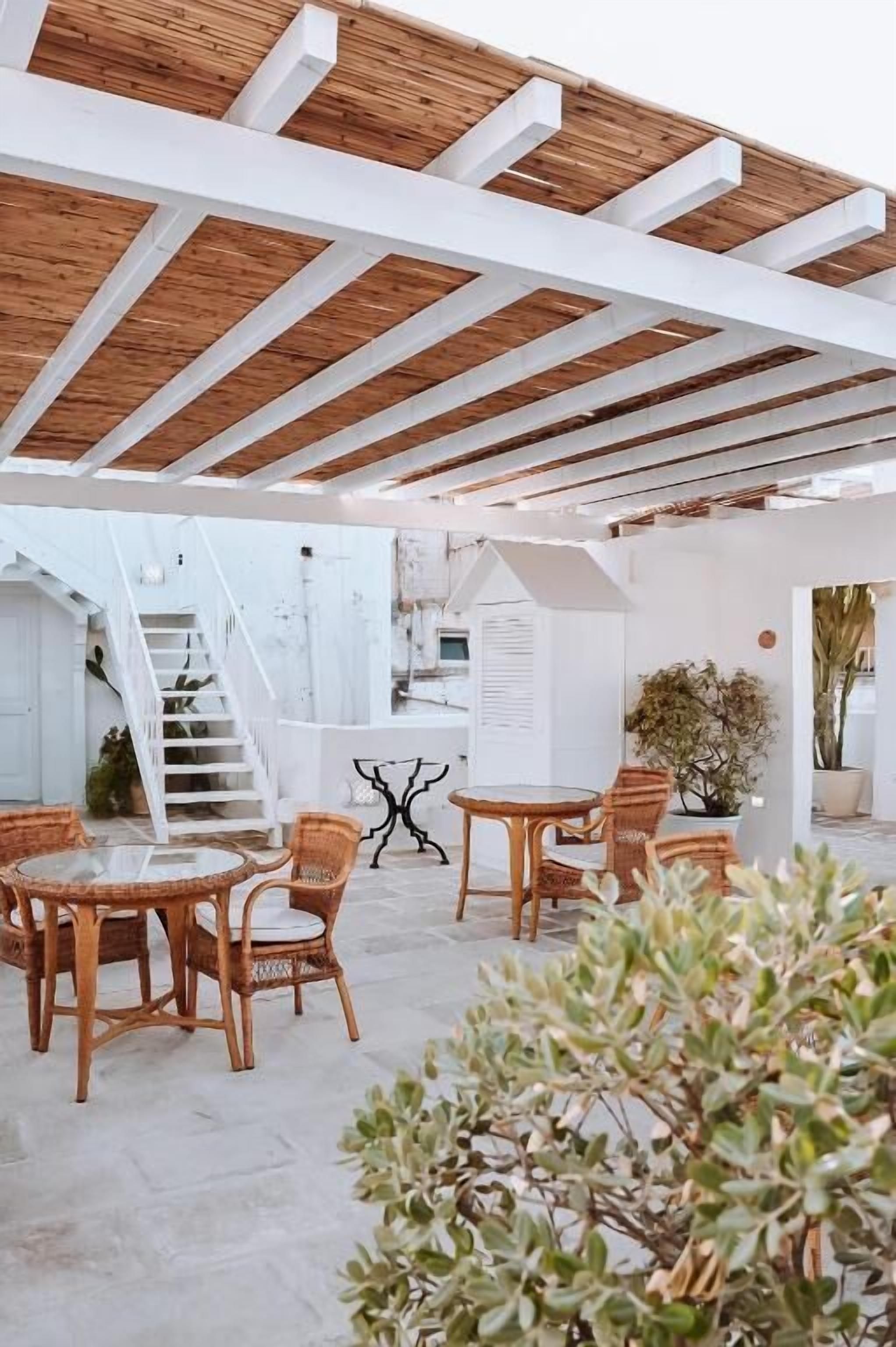 An outdoor patio with wooden beams, wicker furniture, and potted plants.