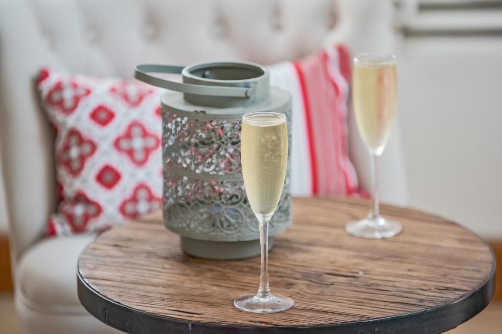 Une table ronde en bois, avec deux coupes à champagne et un pichet décoratif en métal.