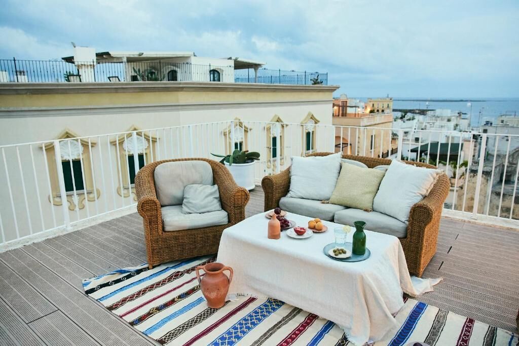 Un balcón con mobiliario de mimbre, una mesa con mantel blanco y vistas a la ciudad.