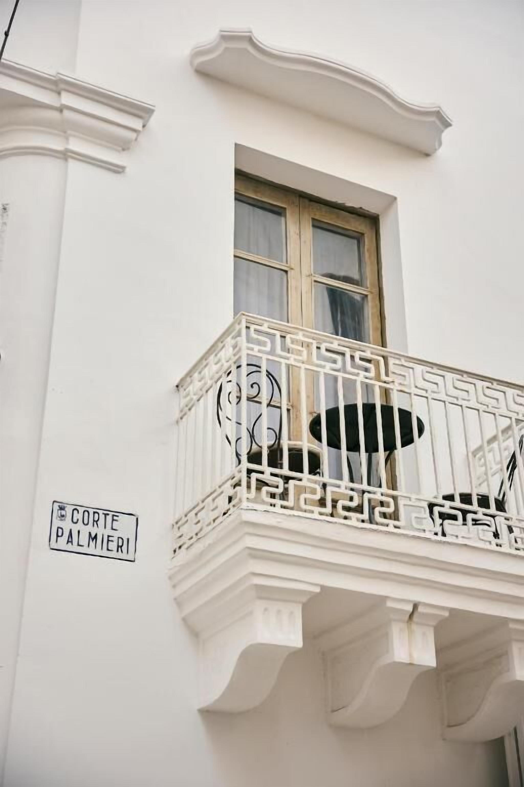 Un bâtiment blanc doté d’un balcon orné d’une balustrade en fer forgé et d’une enseigne indiquant « Corte Palmieri ».