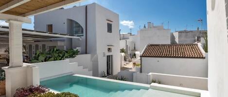 A rooftop pool area with a modern pool, white walls, and a wooden pergola.