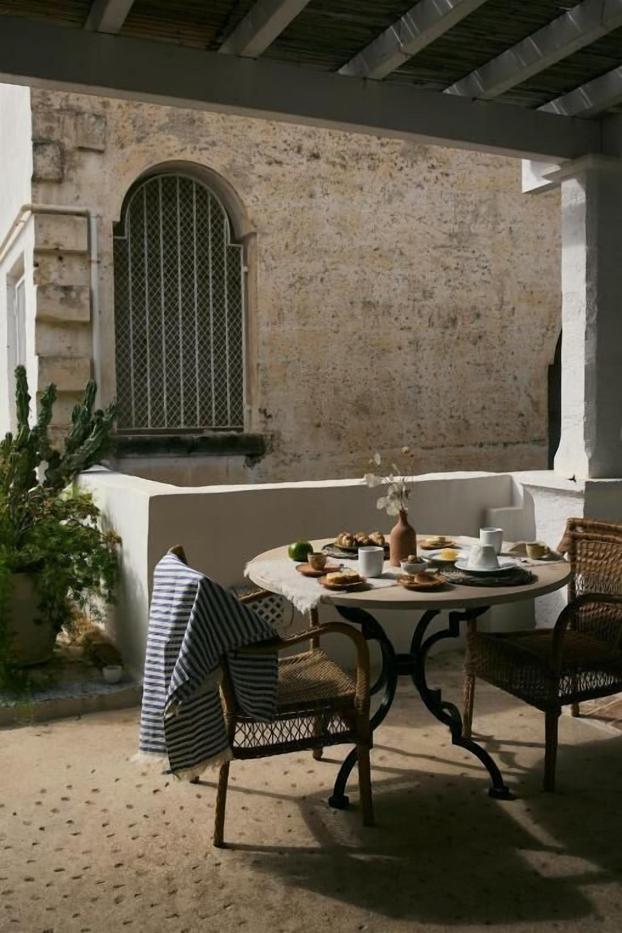 An outdoor dining area with a round table, two wicker chairs, and a white tablecloth.