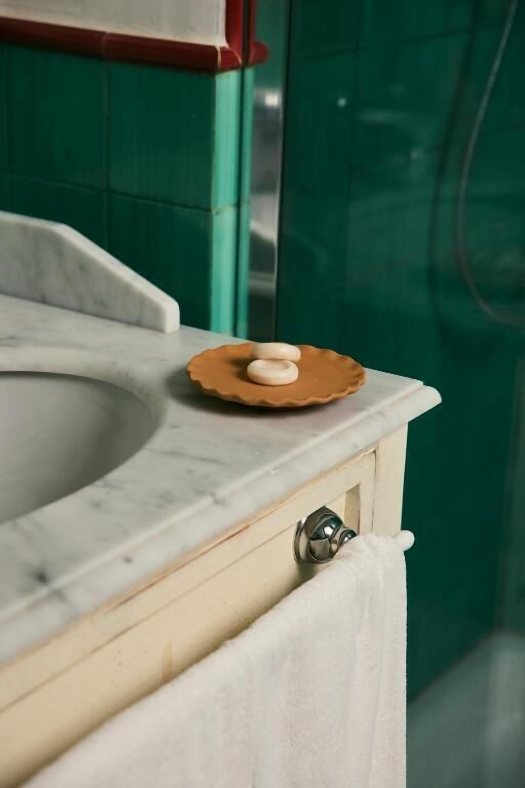 A bathroom with a marble sink, a soap dish, and a towel hanging on a cabinet.