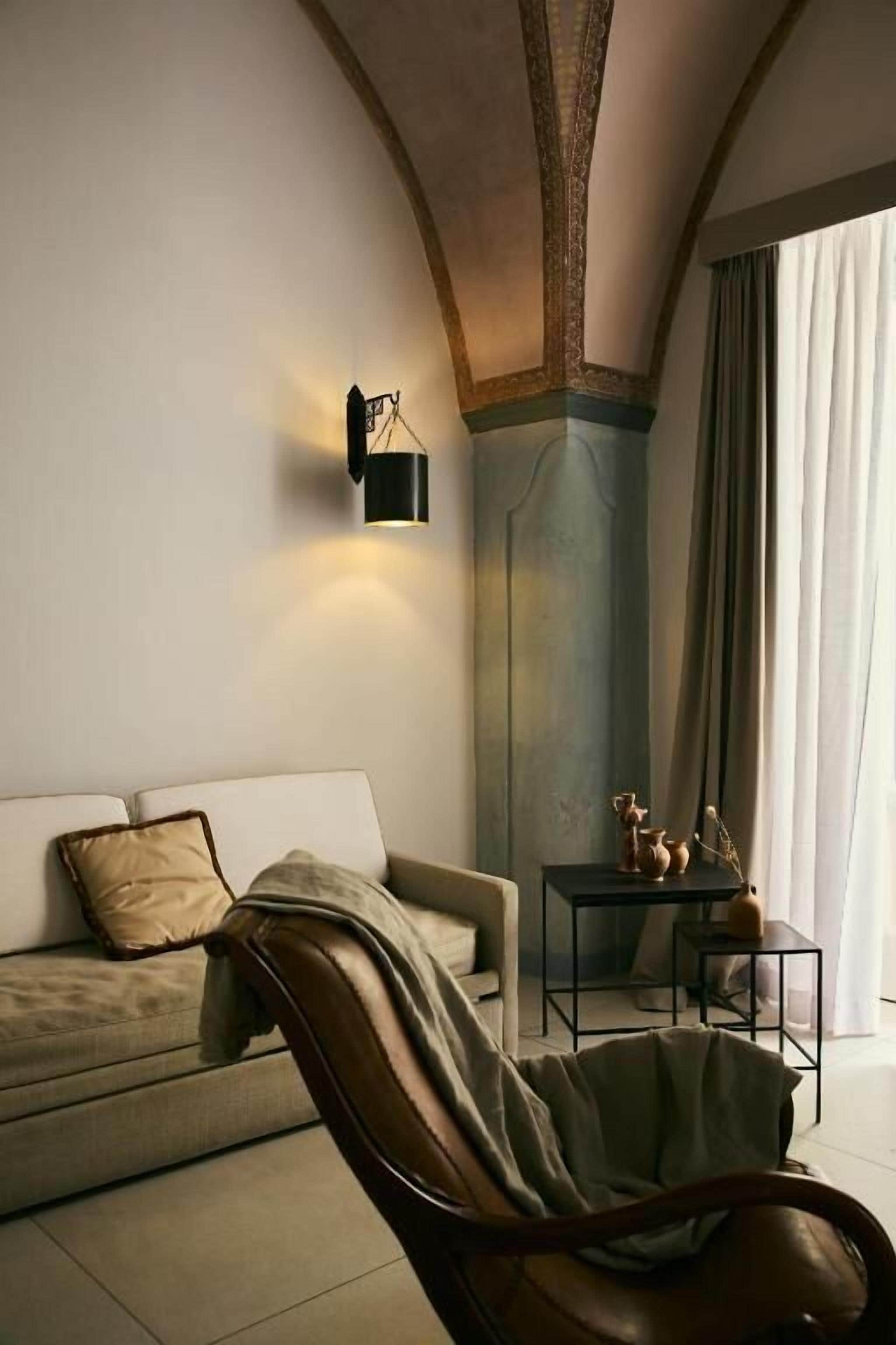 Un salon comprenant un canapé, un fauteuil en cuir, une petite table agrémentée d’objets décoratifs et un luminaire fixé au mur.