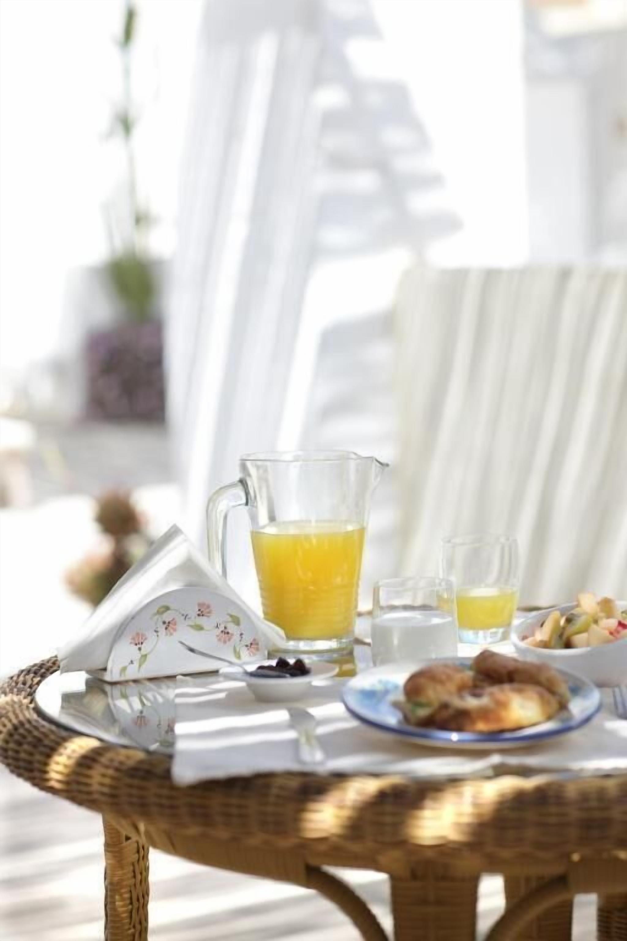 Una mesa de mimbre con una jarra de vidrio con jugo de naranja, un cuenco pequeño y un plato con comida.
