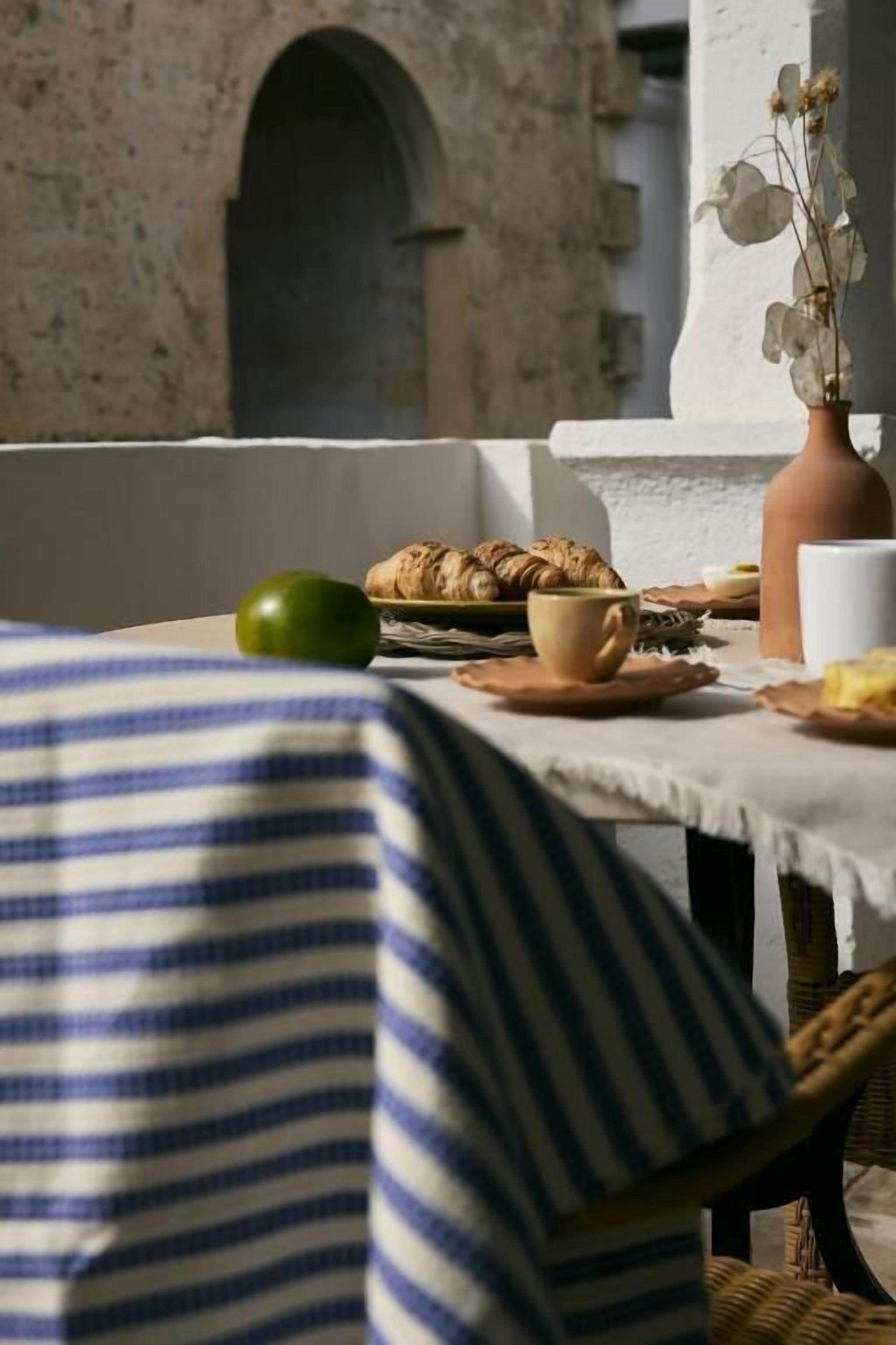 A table set with croissants, a green apple, and a cup, with a view of a stone building in the background.