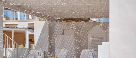 A sunlit outdoor seating area with white planters and a pergola providing shade.