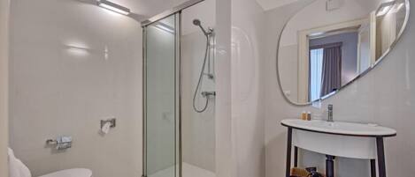 A modern bathroom with a glass-enclosed shower, a white sink with a mirror, and a small vanity with a basket.