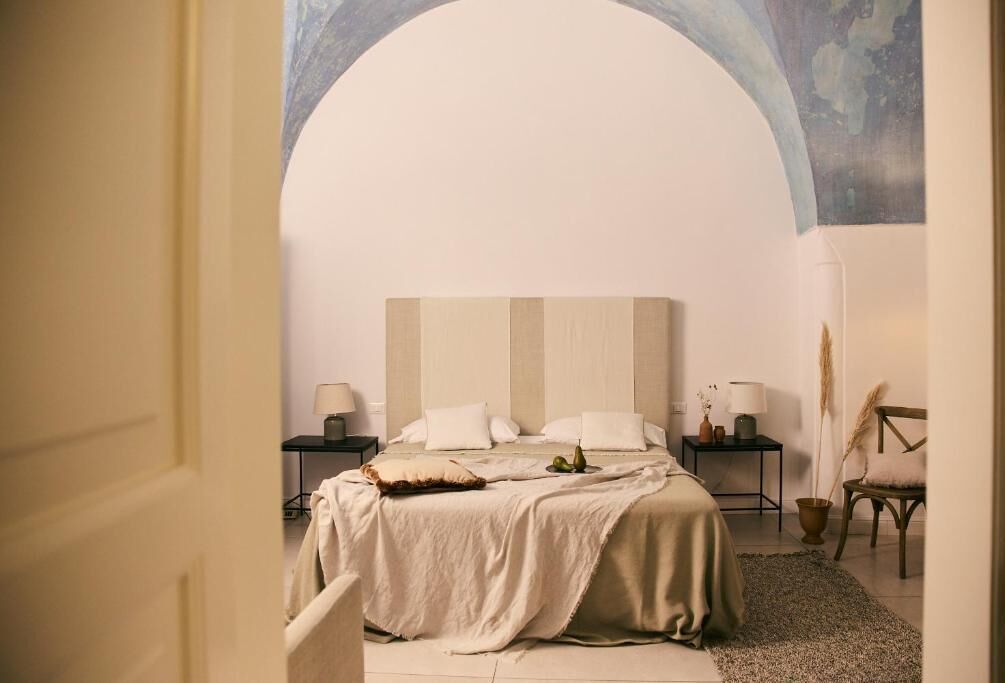 A bedroom with a large bed, a nightstand, a chair, and a wall arch.