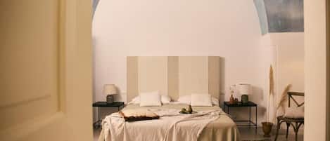 A bedroom with a large bed, a nightstand, a chair, and a wall arch.