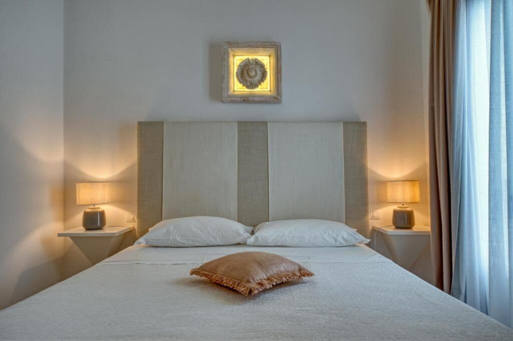 Een net opgemaakt bed met twee kussens, een sierkussen en twee bedlampjes aan beide zijden.