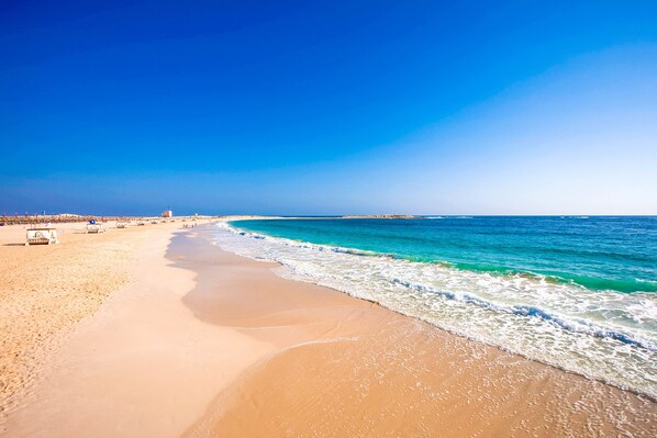 A beach with a clear sky, sandy shore, and a few beach chairs.