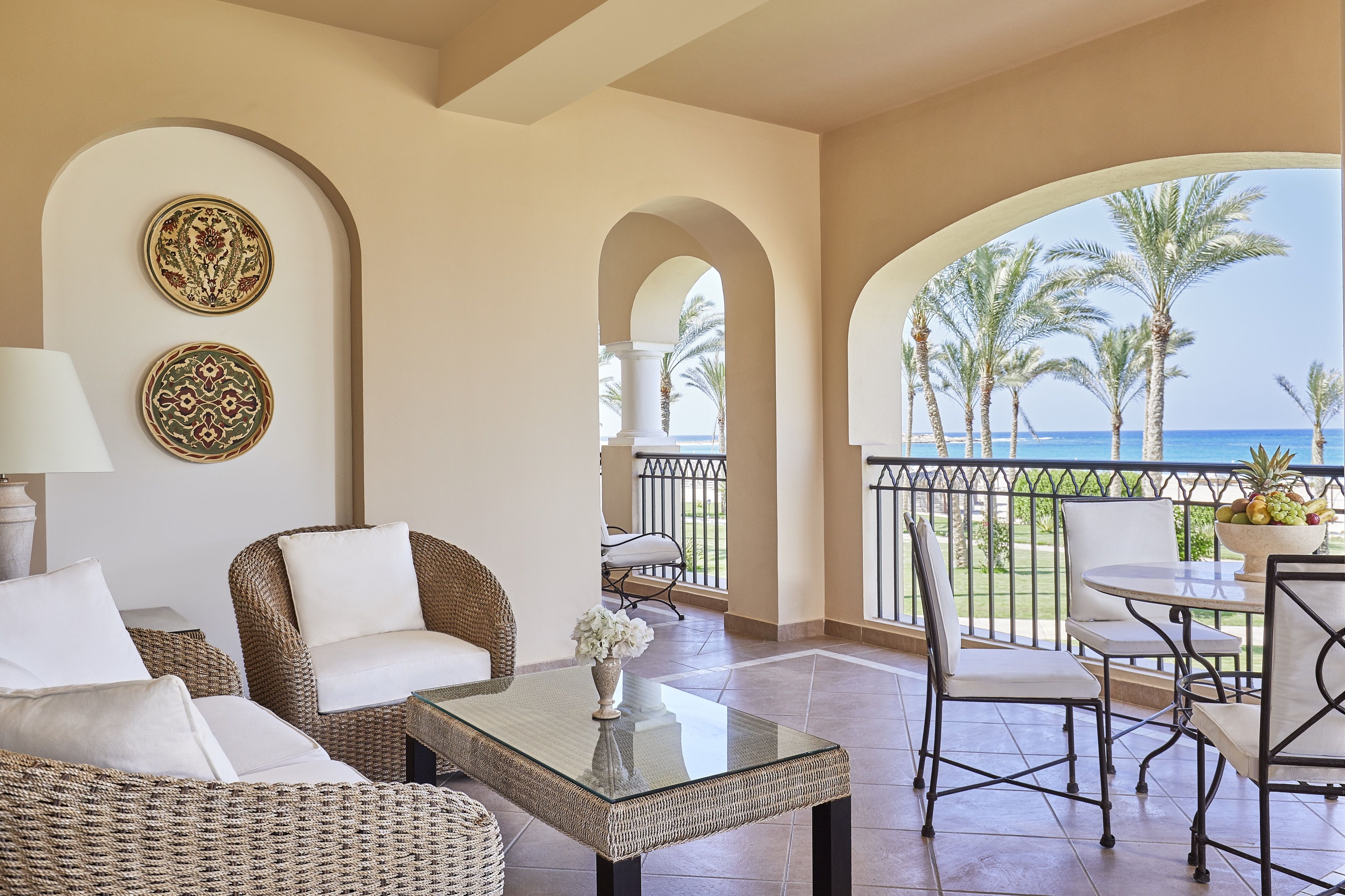 A balcony with wicker furniture, a glass table, and a view of the sea.